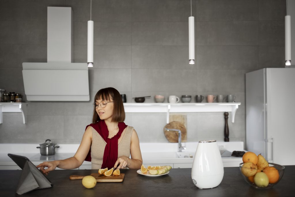 Mulher corta frutas enquanto utiliza um tablet em uma cozinha moderna e bem iluminada. A imagem demonstra como a cozinha pode ser um ambiente multifuncional, combinando praticidade e estilo no dia a dia.
